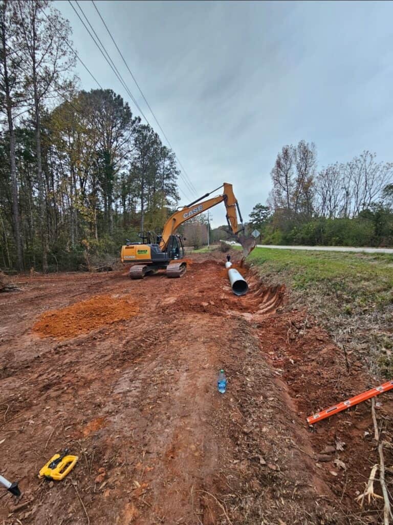 Excavator installing drainage pipe on construction site for land management.