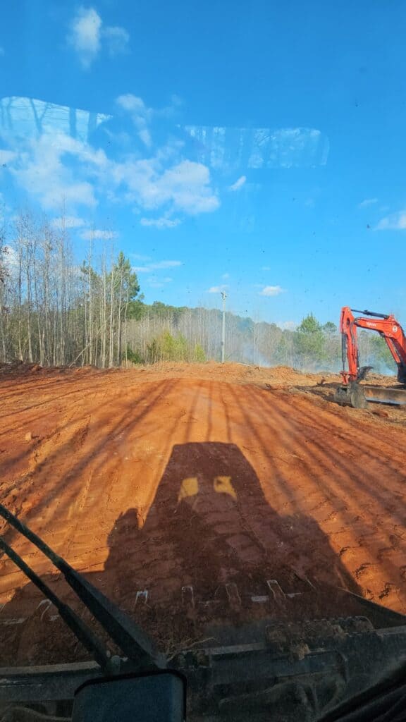 View of land clearing with excavator on dirt road under blue sky.
